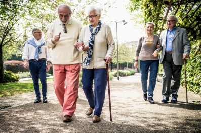 fünf ältere Personen gehen einen Weg entlang. Zwei Päärchen gehen Arm in Arm und ein Mann läuft alleine. 