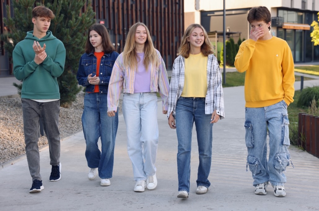 drei Mädchen und zwei Jungs im Teenageralter gehen eine Strasse entlang und unterhalten sich. 